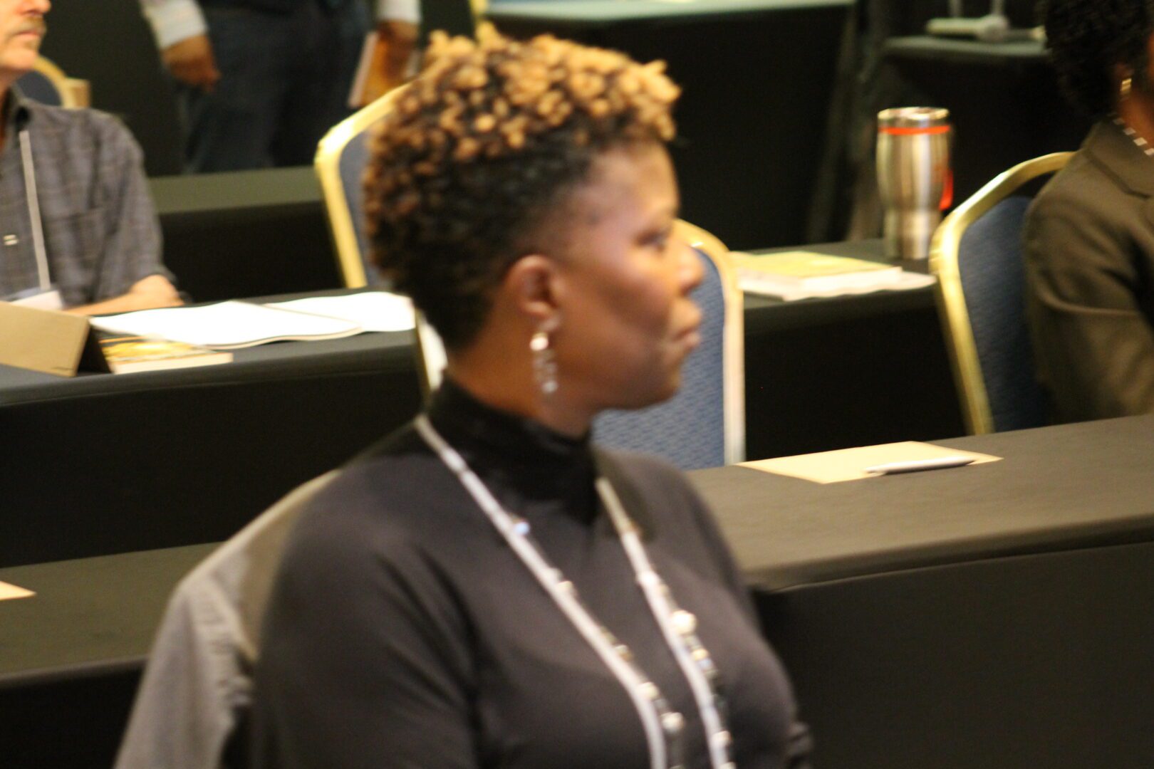 A woman with short hair sitting in front of some chairs.